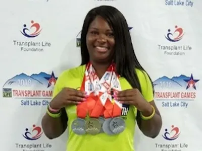 A woman proudly displaying her medals in front of a wall.