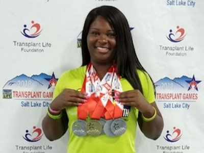 A woman proudly displaying her medals in front of a wall.