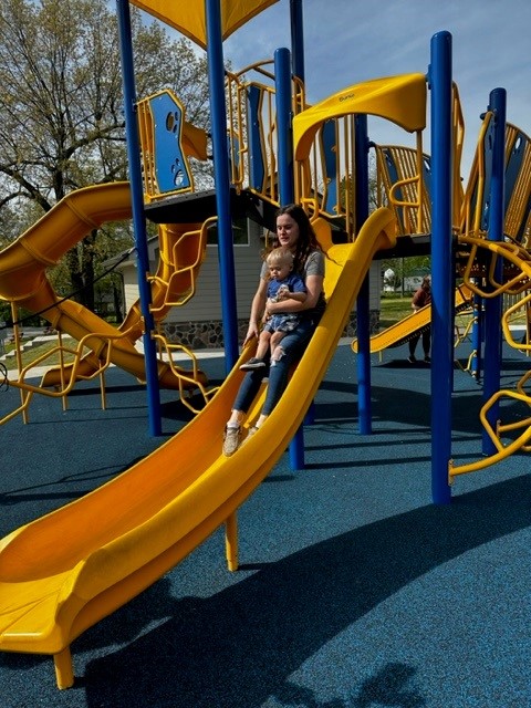  A woman and child joyfully sliding down a playground slide, enjoying a playful moment together.