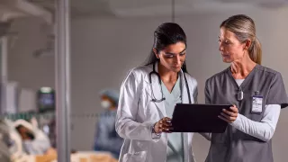 Two healthcare professionals look at a tablet device 