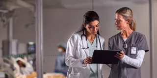 Two healthcare professionals look at a tablet device 
