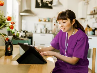 A woman in purple scrubs focused on her laptop, engrossed in her work